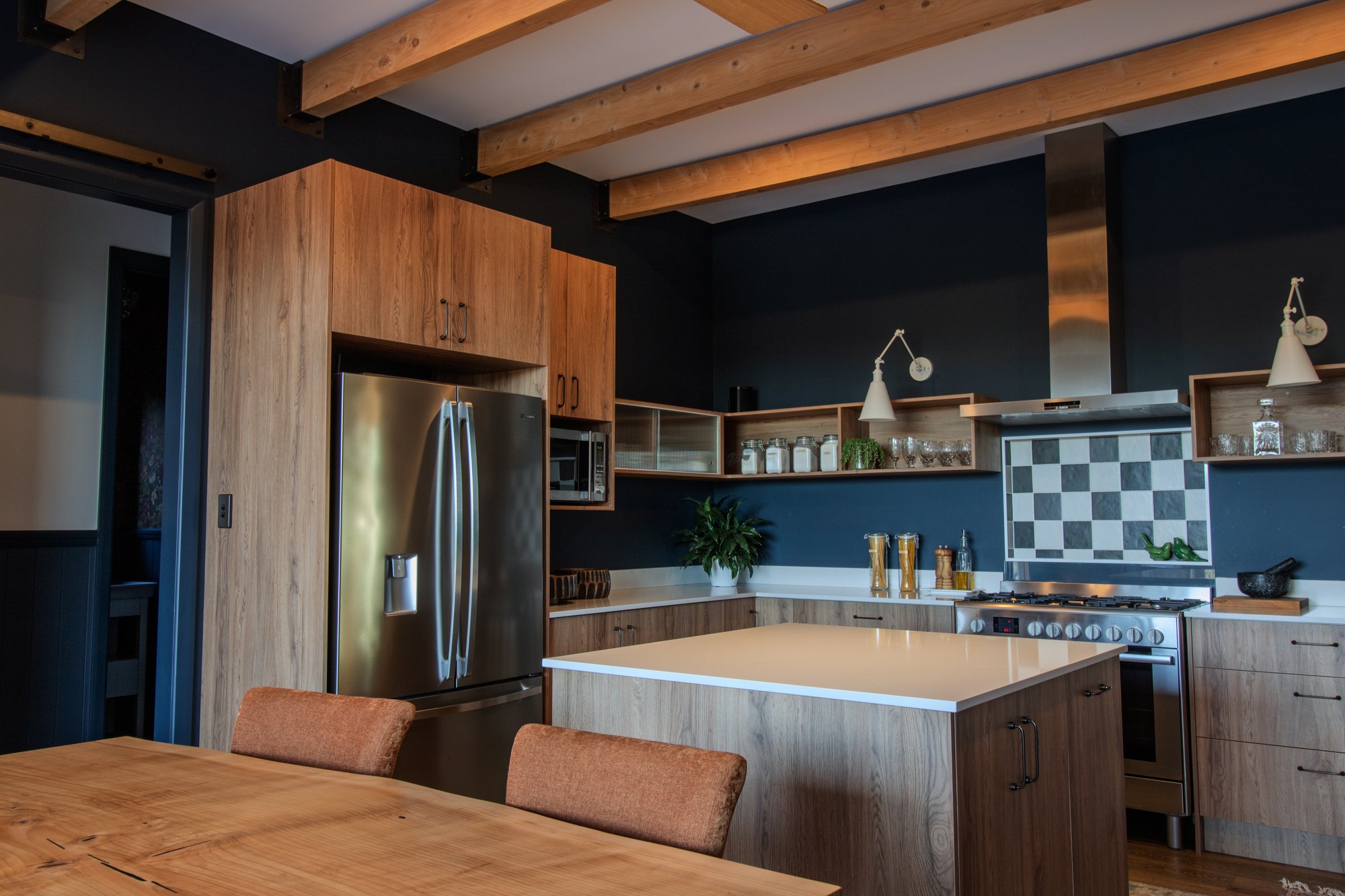 Kitchen island, custom cabinetry and gas cooktop beneath exposed timber beams and deep blue walls