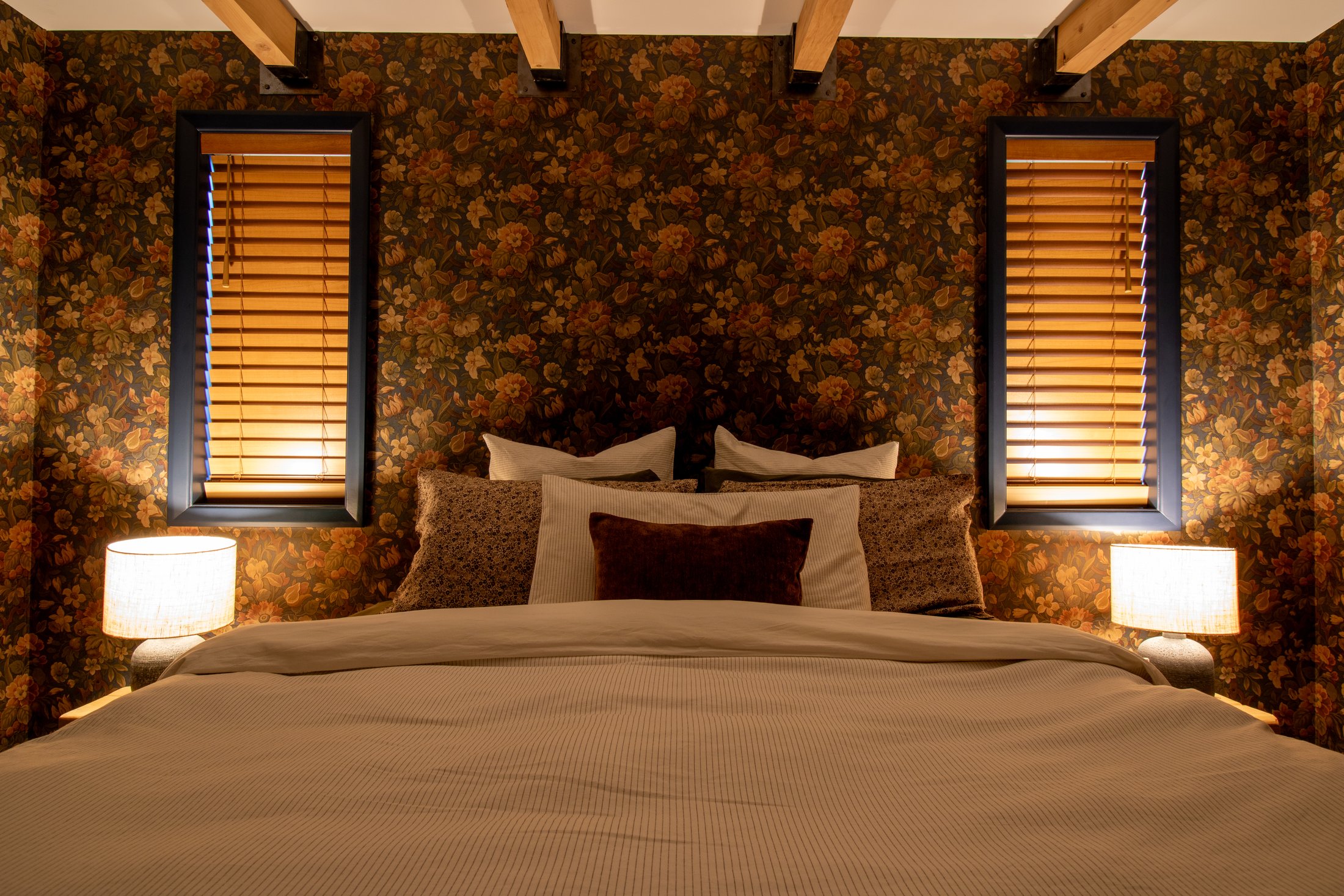 Master suite with patterned wallpaper, exposed timber beams and upholstered headboard
