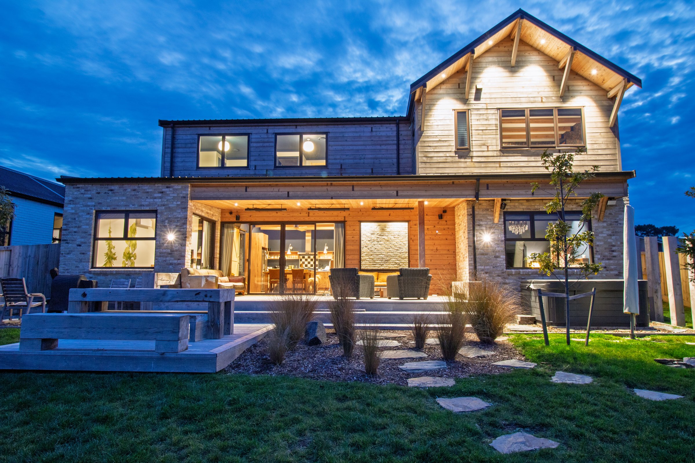 Rear elevation at dusk with the covered alfresco, spa patio and macrocarpa decking lit for evening